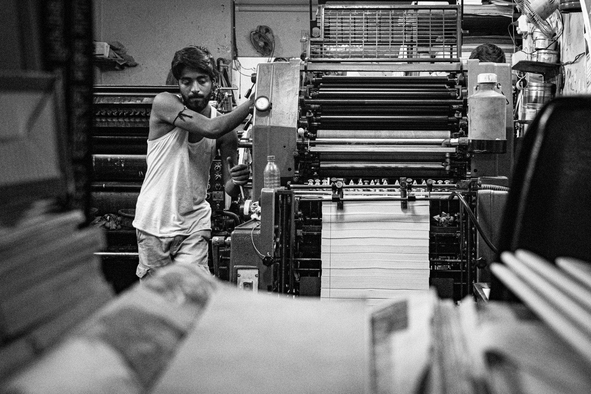 Industrial print shop scene with a worker operating a vintage printing press in black and white.